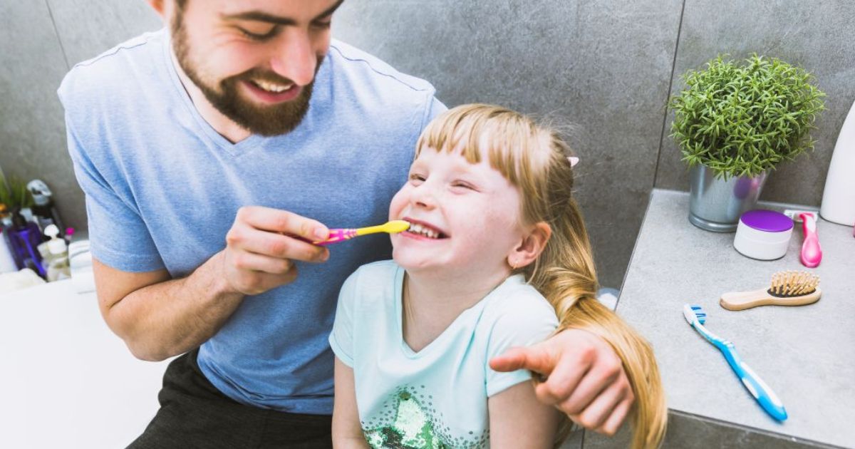 Young child brushing teeth with parent helping in bright bathroom, morning routine, teaching independence and healthy habits