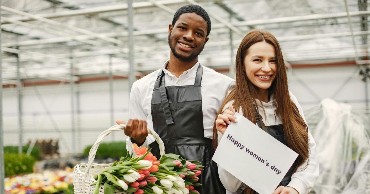 Beginner gardeners smiling while planting tomatoes in raised beds