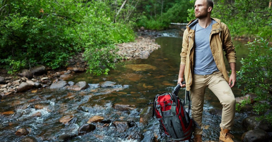 Person walking on sunlit forest path with reusable water bottle, starting affordable zero waste journey"