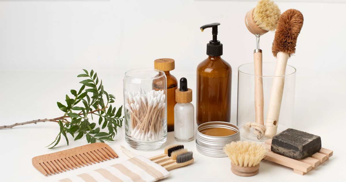 Safety razor, shampoo bars, bamboo toothbrush, and refillable glass bottles on bamboo tray with plant, plastic-free bathroom gift ideas