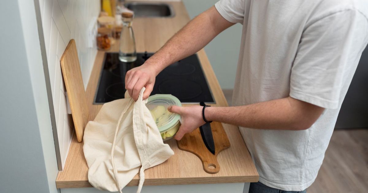 "Minimalist zero waste kitchen with glass jars on open shelves, beeswax wraps, stainless steel containers, wooden utensils, and countertop compost bin, organized sustainable American home 2026"