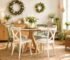 Bright dining room with a wooden table, light-colored chairs, decorative wreaths, and plants.