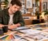 Person planning an interior with a laptop, color samples, drawings, and material references on a table.