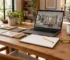 Interior planning desk with laptop showing generic simple 3D room view without readable UI, physical tape measure, pencil and blank sketchbook